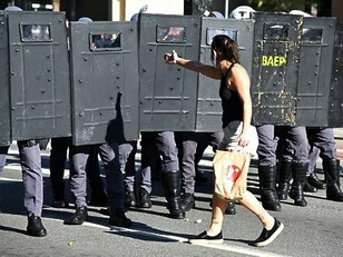 Frente a frente com o cordão policial, a manifestante simboliza o encontro entre a expressão do dissenso e os mecanismos institucionais de manutenção da ordem. O artigo propõe refletir sobre as disputas políticas e epistemológicas que moldam o mundo contemporâneo
