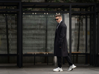 A modern man in a black coat and sneakers standing confidently on a city street