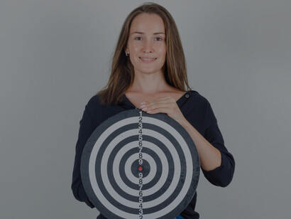 A young woman in a black shirt pointing at a dartboard, symbolizing actionable goals and an action plan