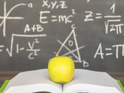 Opened book with apple on desk near chalkboard