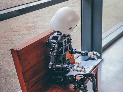 A harmless AI prototype is sitting on a bench and ironically using technology because we are in the digital era