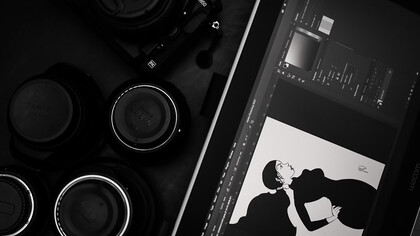 A black and silver DSLR camera placed beside a tablet, where someone is drawing—capturing a moment of creativity in action