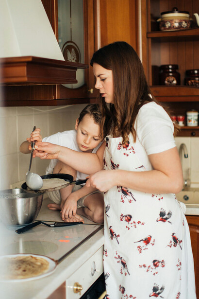 A mother cooks crepes with her child, capturing a moment of shared domestic routine