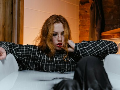 A woman sits in a dimly lit bathtub, with a distant gaze and a disheveled appearance speaking volumes about inner turmoil. This image captures the silent struggles of modern life, where relentless competition and unquenchable greed often leave individuals overwhelmed, contributing to a surge in mental health challenges like depression