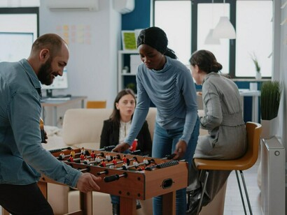 A diverse group of colleagues playing foosball, enjoying drinks, and sharing snacks in the office after work, reflecting a shift in workplace culture