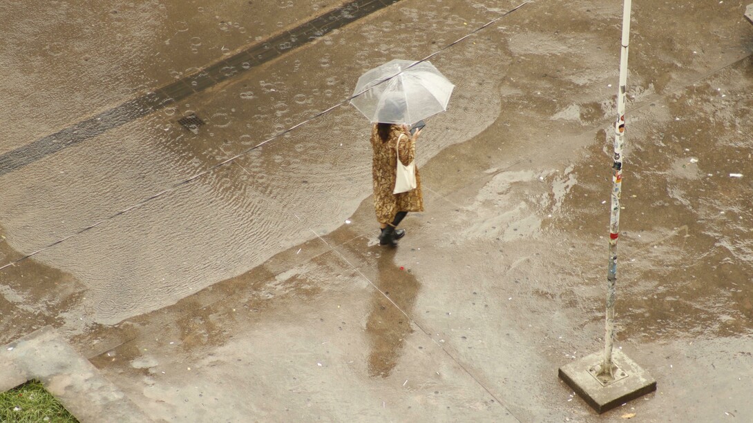 A woman walking alone through the city on a rainy day, sheltered beneath an umbrella