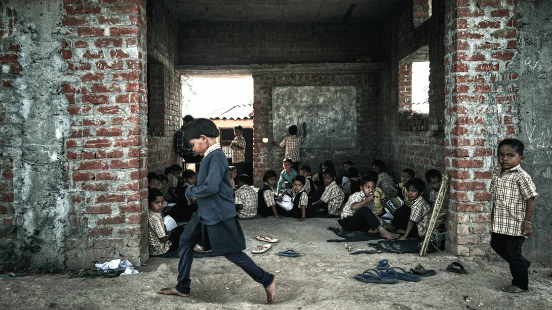 A group of children in school uniforms sit on the dusty floor of an unfinished brick building, a powerful reminder of the urgent need for global efforts to ensure equal opportunities for all