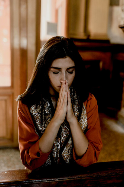 A brunette woman praying while kneeling inside a church