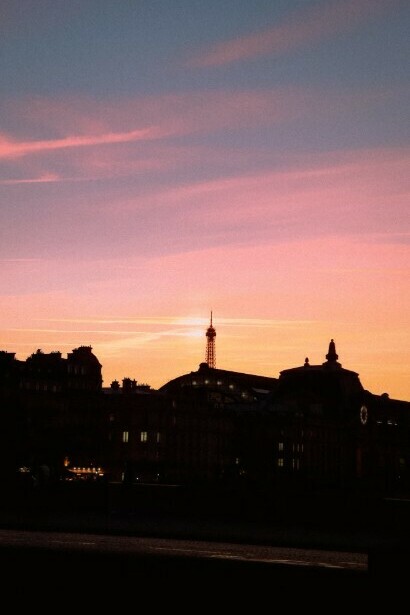 A Parisian street at dusk, with soft pink clouds in the sky and a streetlight glowing on the sidewalk,France