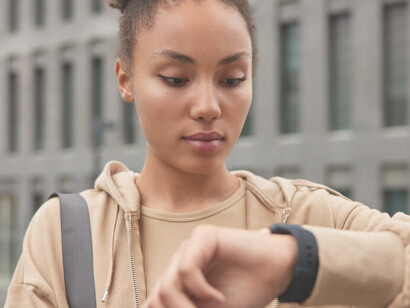 A fitness model, sporting a beige sweatshirt, checks her workout results on a smartwatch after outdoor exercise, demonstrating the integration of wearable devices and smart technology in fitness