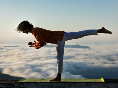 Man practicing yoga on the edge of a building with the sky behind him