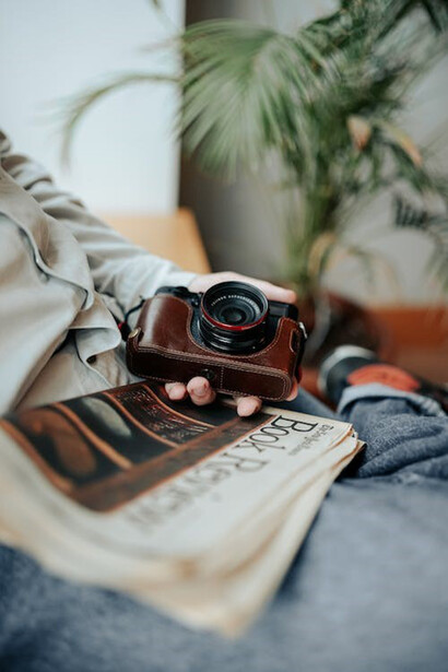 A man poised with a retro analog camera, holding a newspaper