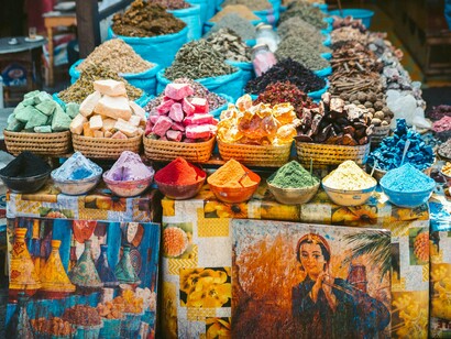 Feira de rua em Marraquexe. As ruas estão imersas numa paleta de cores quentes, com a arquitetura única da cidade, que mistura o antigo e o moderno