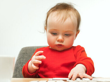 A happy toddler girl sits at a computer keyboard, showcasing her curiosity as she explores technology and engages with the digital world