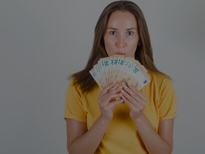 A young woman wearing a vibrant yellow t-shirt beams with happiness as she enthusiastically points at a pile of euro banknotes
