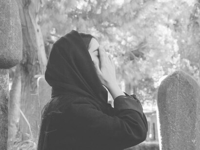 A woman placing her hands on her face in pain at the cemetery 