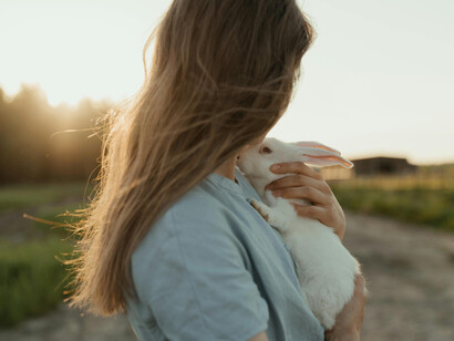 A young woman on a field, holding a white rabbit, looking at the horizon