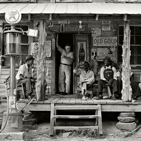 Dorothea Lange, Negozio di campagna su strada sterrata. Domenica pomeriggio. Si noti la pompa del cherosene a destra e quella della benzina a sinistra. I pali di legno grezzi e non rifiniti sono stati usati come sostegno per il tetto della veranda. Uomini neri sono seduti sulla veranda. Il fratello del proprietario del negozio è in piedi sull'ingresso - Gordonton, North Carolina, 1939. Per gentile concessione di Anna Defrancesco