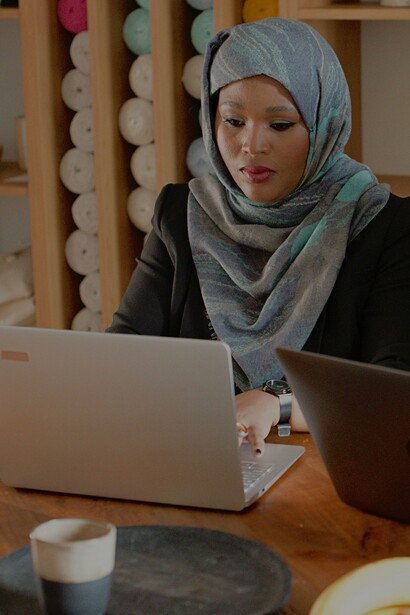 Mulher de hijab cinza e verde usando um laptop