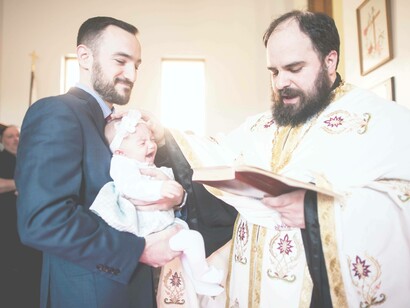 The godfather is in attendance during this baptism ceremony in which the baby is in mid-scream-and-cry