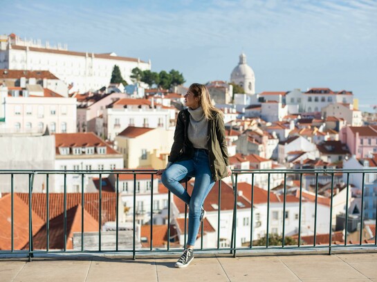 
A woman sitting on metal railings and watching the scenery in Lisbon, Portugal
