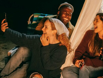 Friends smiling at the camera as they take a selfie, illustrating how photographs become living memories