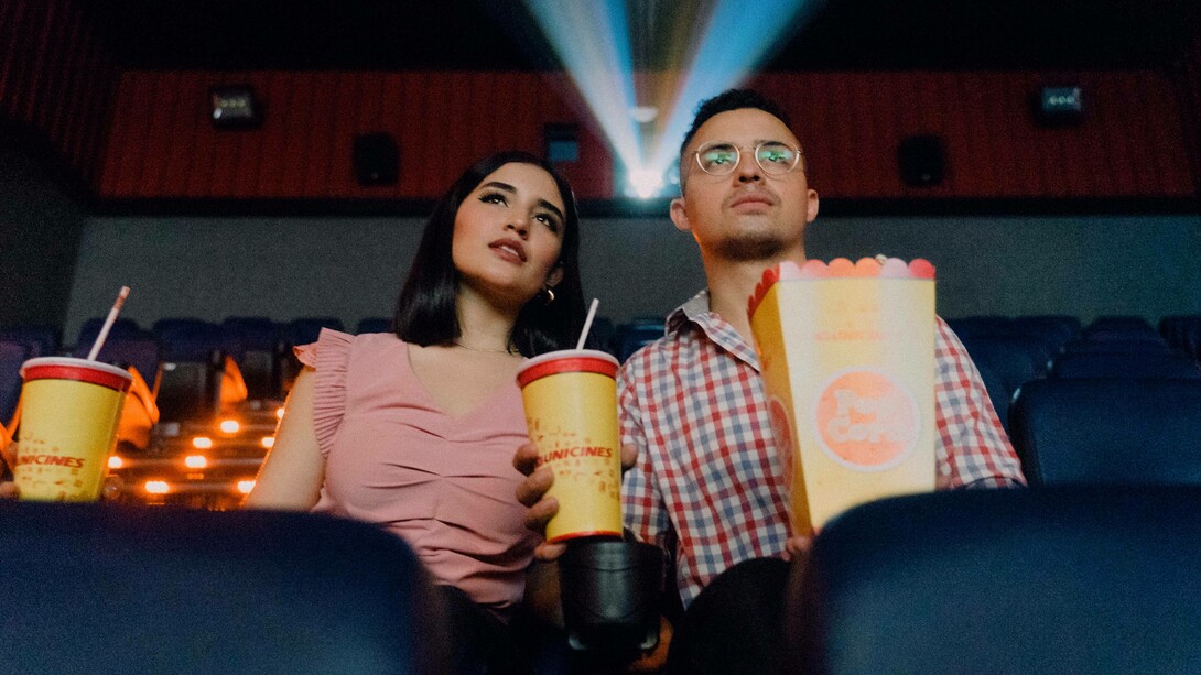 A couple at the cinema have their popcorn and drinks and are eagerly anticipating the movie they are about to watch