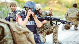 Correspondente de guerra tira fotos enquanto soldados a protegem