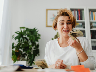 A woman struggles to pay household bills, counting money as she becomes overwhelmed by financial stress
