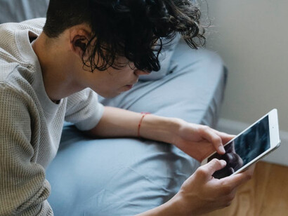 Ragazzo sul proprio letto con gli occhi fissi sul cellulare 