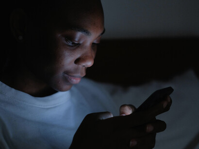 Woman using her phone at night in a dark room, surrounded by glowing screens