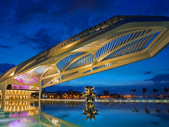 O Museu do Amanhã se projeta sobre o espelho d’água da Praça Mauá, iluminado contra o céu azul do início da noite. A arquitetura de Santiago Calatrava transforma o edifício em um dos símbolos mais marcantes do Rio de Janeiro contemporâneo