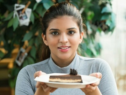 A young Indian woman holding a creamy pastry in a café, reflecting modern dietary habits linked to increased sugar consumption in India