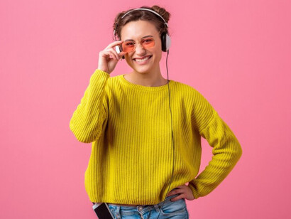 A stylish woman in colorful hipster attire enjoys a trending music track while wearing headphones