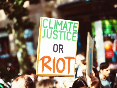 An enviornment protestor not in denial of climate change carrying a sign reading "climate justice or riot"