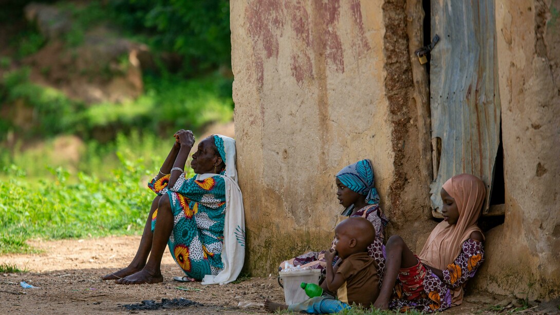 An elderly woman and children sitting on the ground, illustrating the everyday realities of poverty and malnutrition