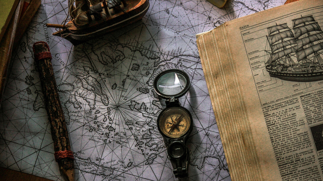 The wooden table, adorned with antique books, vintage marine charts, and a compass, creates a perfect setting for exploring geography and maritime history