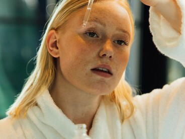 A woman in a white robe carefully applying serum, reflecting the importance of delivering skincare ingredients to the skin in the right way
