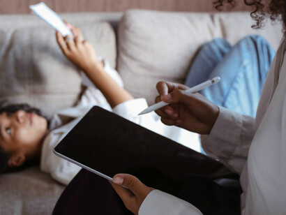 Momento de concentração: uma garota deitada no sofá, explorando suas anotações de leitura ao lado de sua mãe