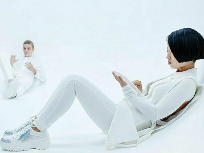 A man and a woman sitting in the room, with their eyes fixed on tablets, representing the modern habit of choosing devices over dialogue