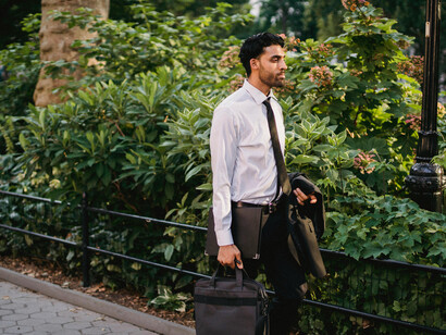 A man in a white long-sleeve shirt and suit sits on a brown wooden bench, looking for a job