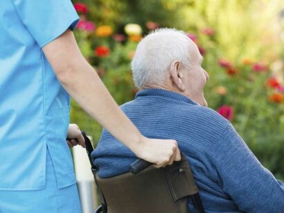 Una cuidadora pasea a un anciano en silla de ruedas