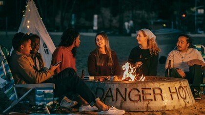 A group of friends sits around a fire pit, sharing stories in a circle during a community storytelling event