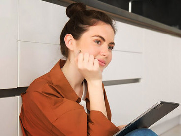 The charm of a young woman lost in reverie as she daydreams while sitting on the kitchen floor at home