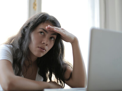 A young woman using her laptop at home, experiencing digital anxiety, information overload, and stress from scrolling the news