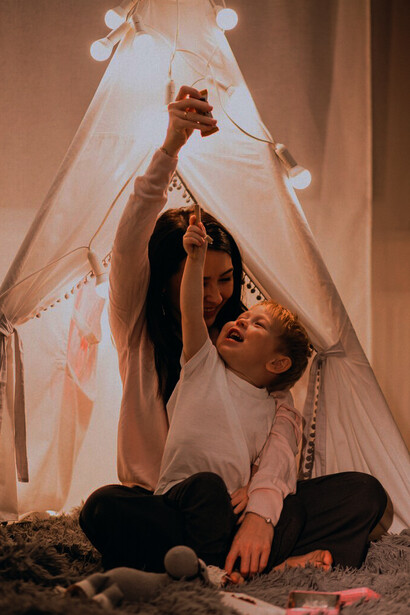 A mother and her son nestled in a warm, glowing tent at home on Christmas, cherishing a quiet moment together