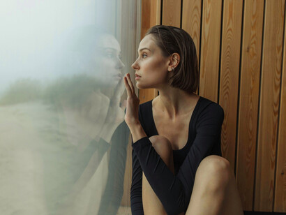 A woman lost in thought while looking beyond the glass, symbolising the longing for clarity that remains just out of reach