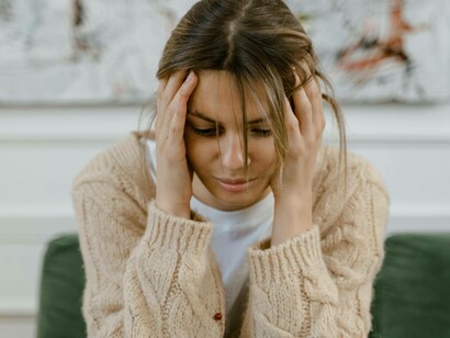 Una donna siede con la testa tra le mani, lo sguardo basso e assente. Le sue mani, che afferrano delicatamente i capelli e la fronte, comunicano un senso di pressione mentale