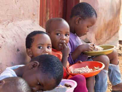 Village children in Africa sharing a meal outdoors, illustrating the struggles of malnutrition and food scarcity