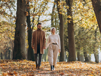 A young couple walking side by side in an autumn park, surrounded by falling leaves and a calm atmosphere
